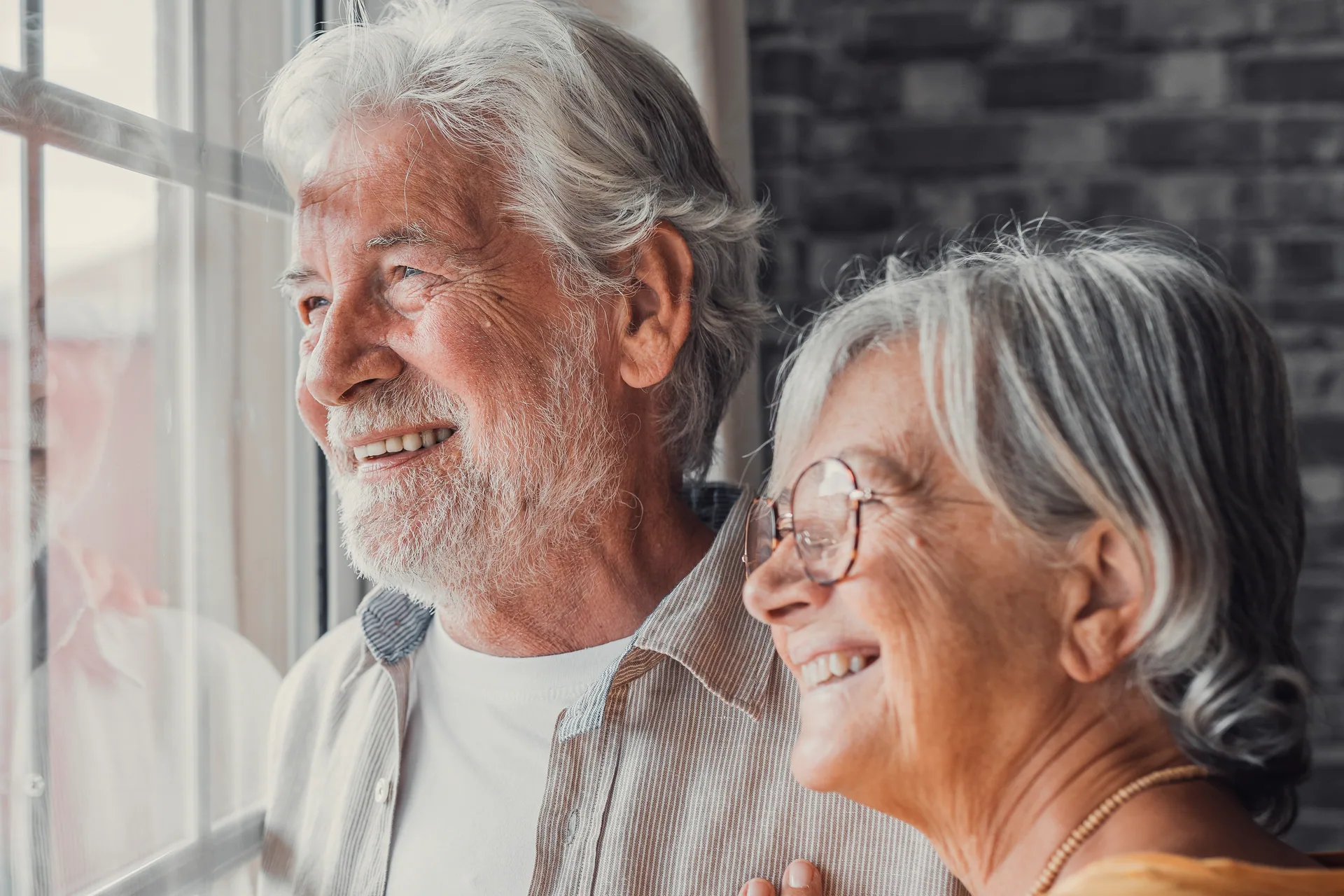 An older couple smiling as they look out of a window together
